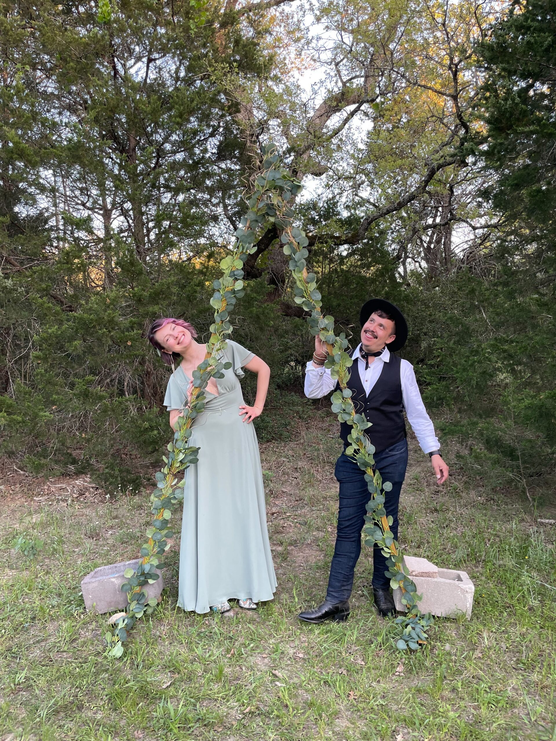 a triangular gold arch with eucalyptus tied to it. Two wedding guests pose behind it. 